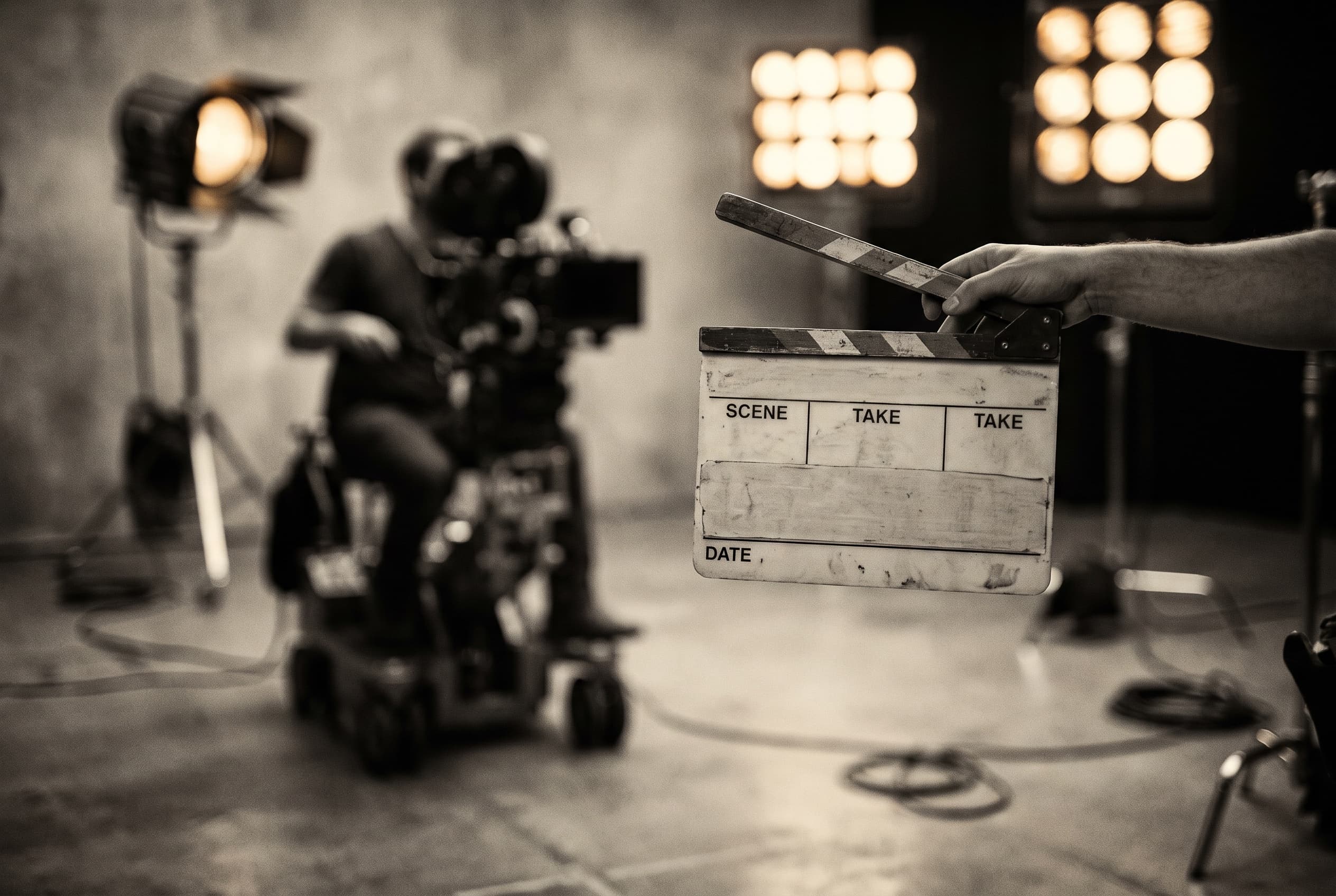 Clapperboard held up before a take, film set lights blurred behind