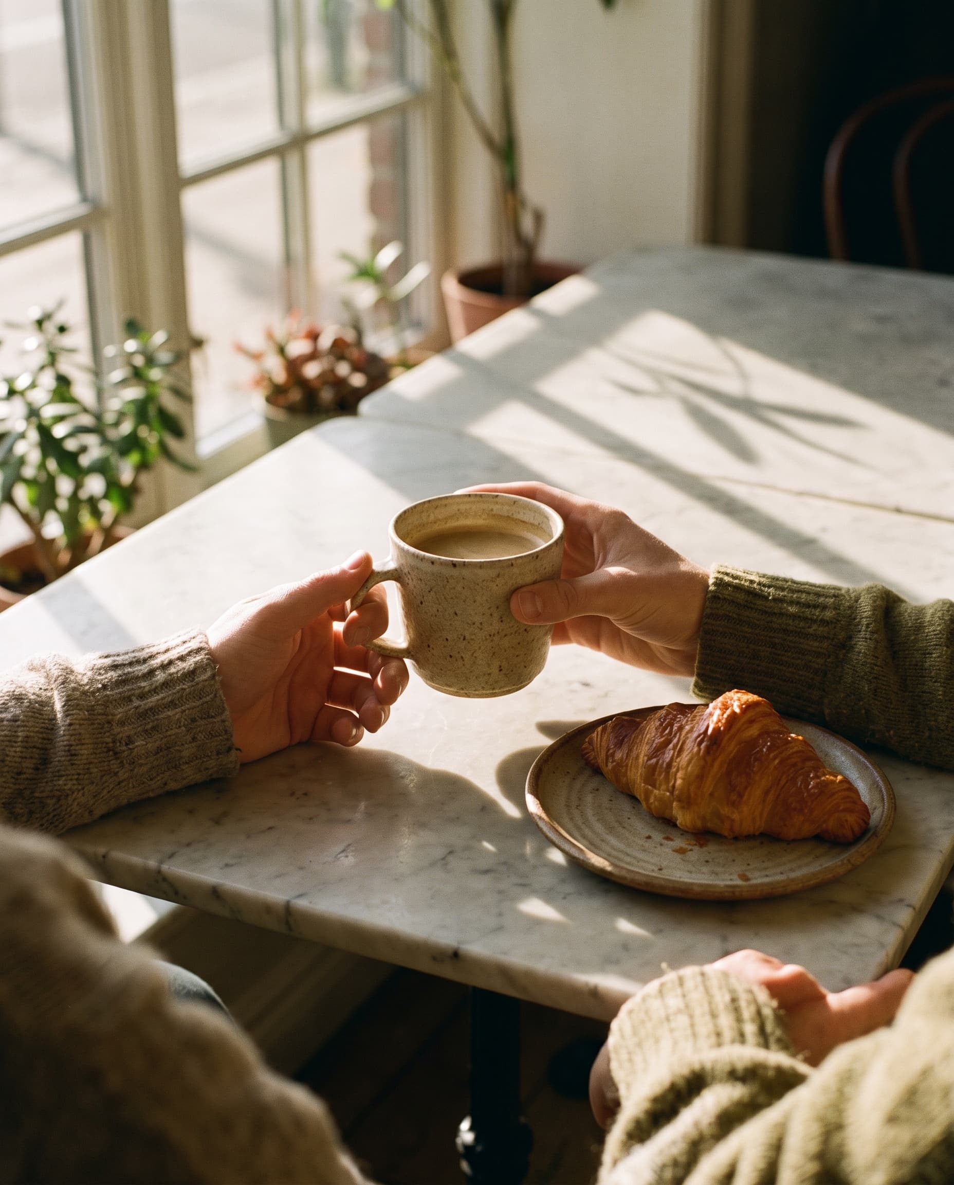 Hands holding a ceramic coffee cup across a marble cafe table in morning light