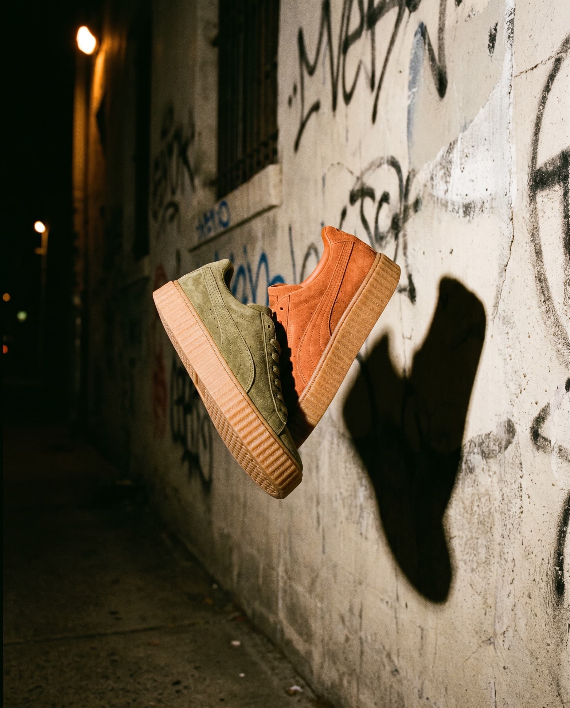 Suede sneakers frozen mid-air against a concrete wall with hard flash